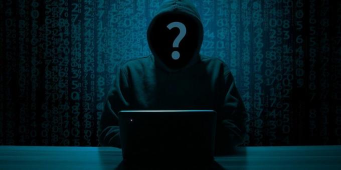 Masanın üzerinde bir PC ile siyah kapüşonlu anonim hacker'ın yüzü